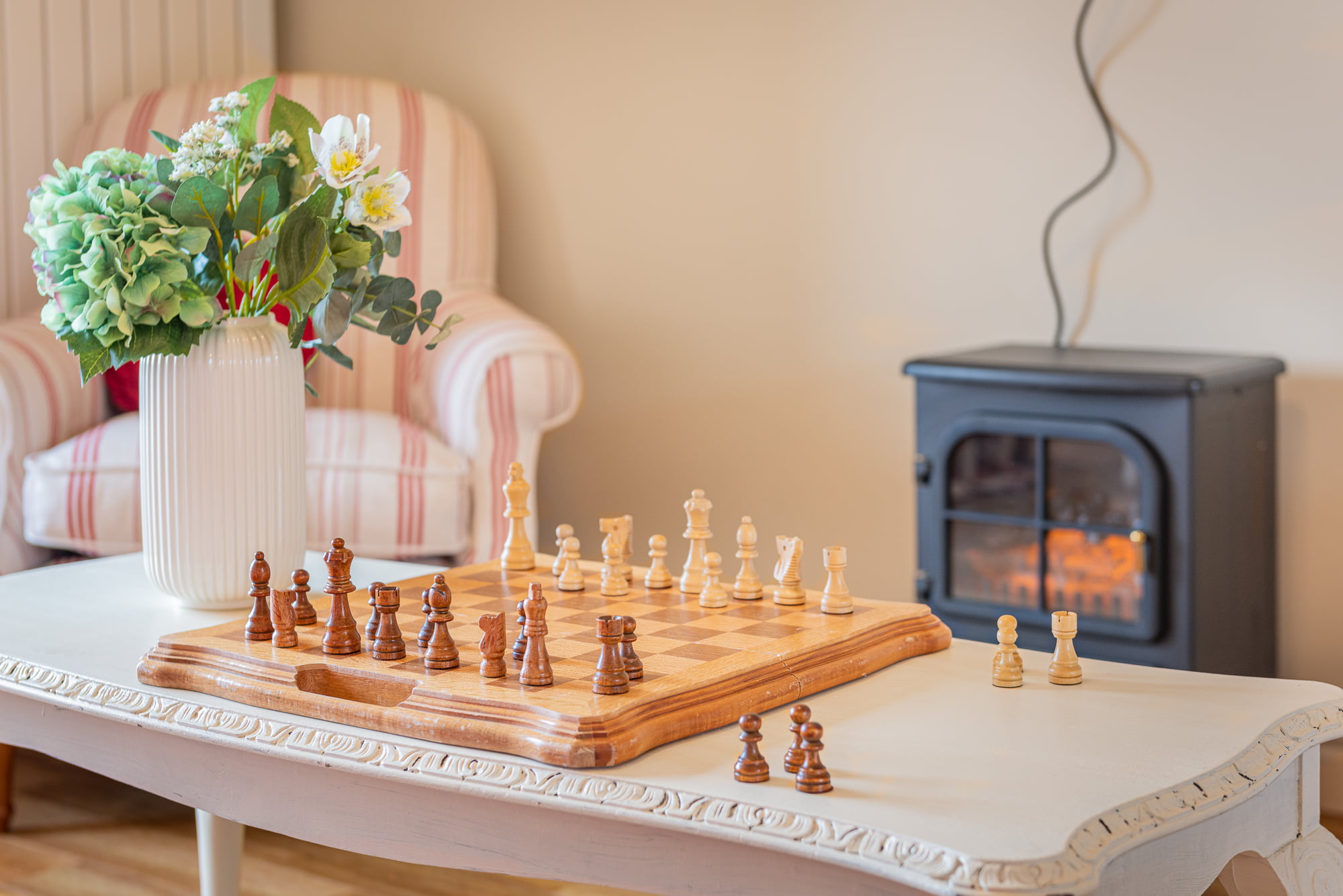 An investment property sold by Currans Homes. The picture features the living room of the property a chess board sits next to a vase of flowers on a white coffee table. In the background an electric fire.